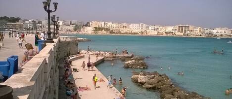 A coastal promenade with people walking and swimming.