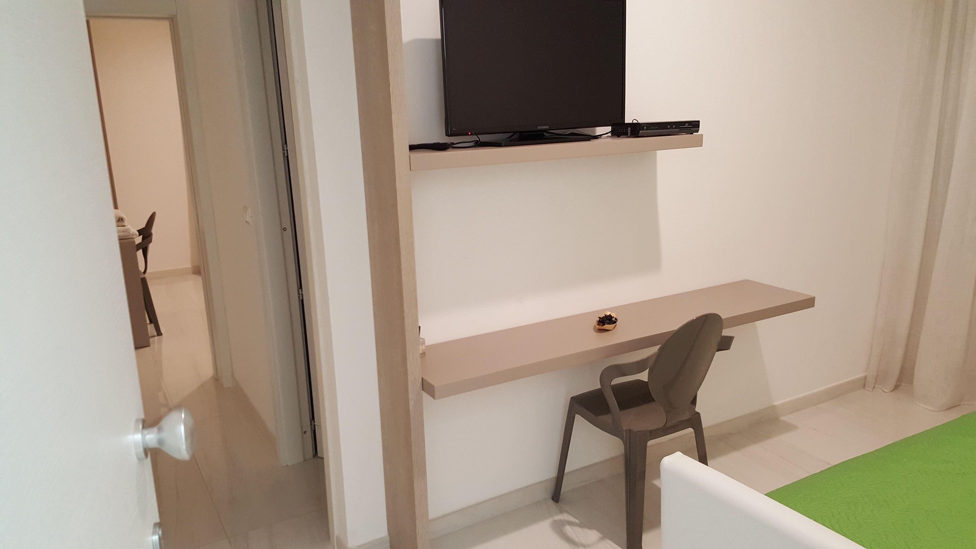 A room with a desk, chair, and a flat-screen TV mounted on a wall.
