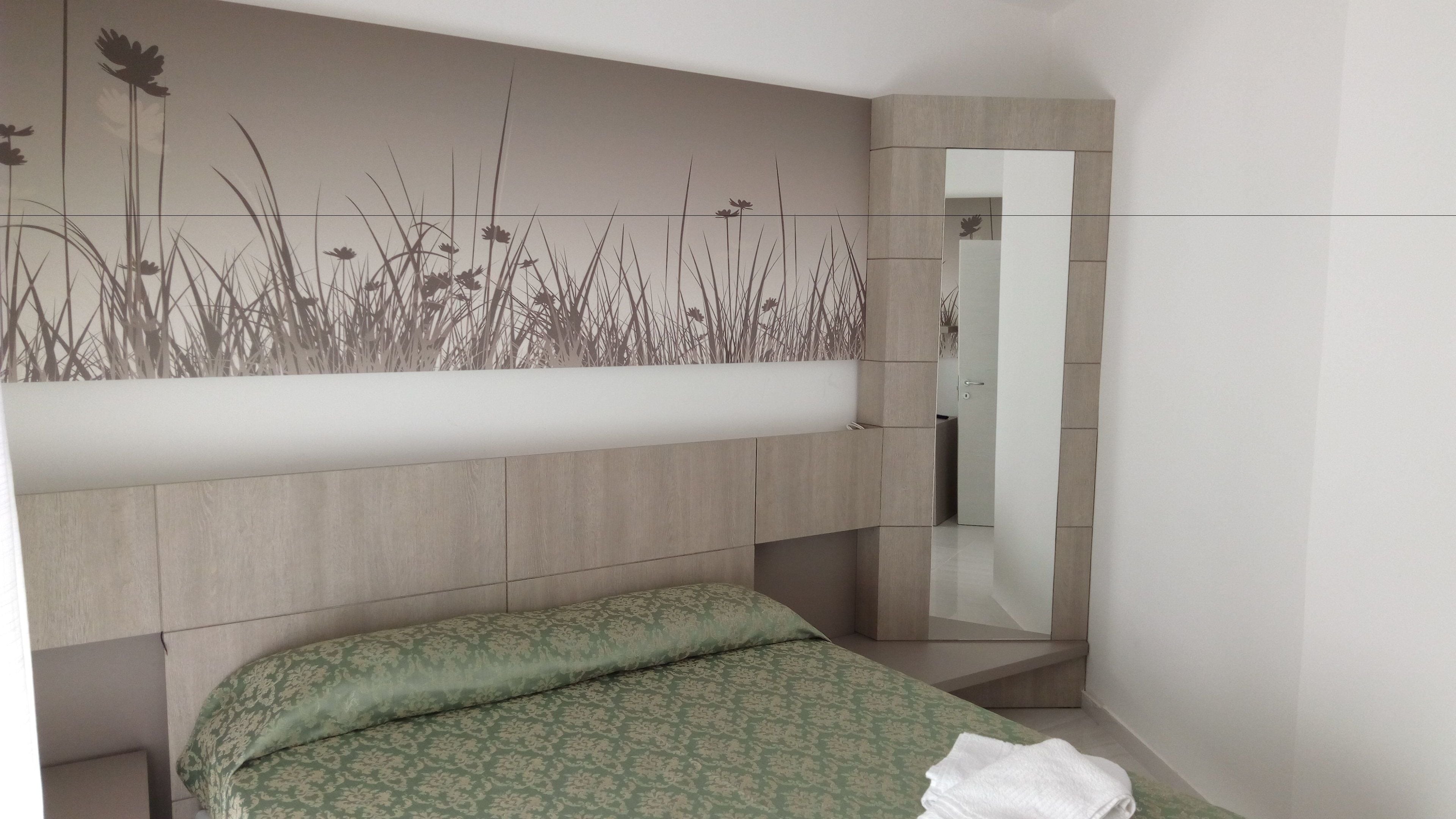Une chambre à coucher comprenant un lit, un miroir et un mur décoré avec un motif inspiré de la nature.