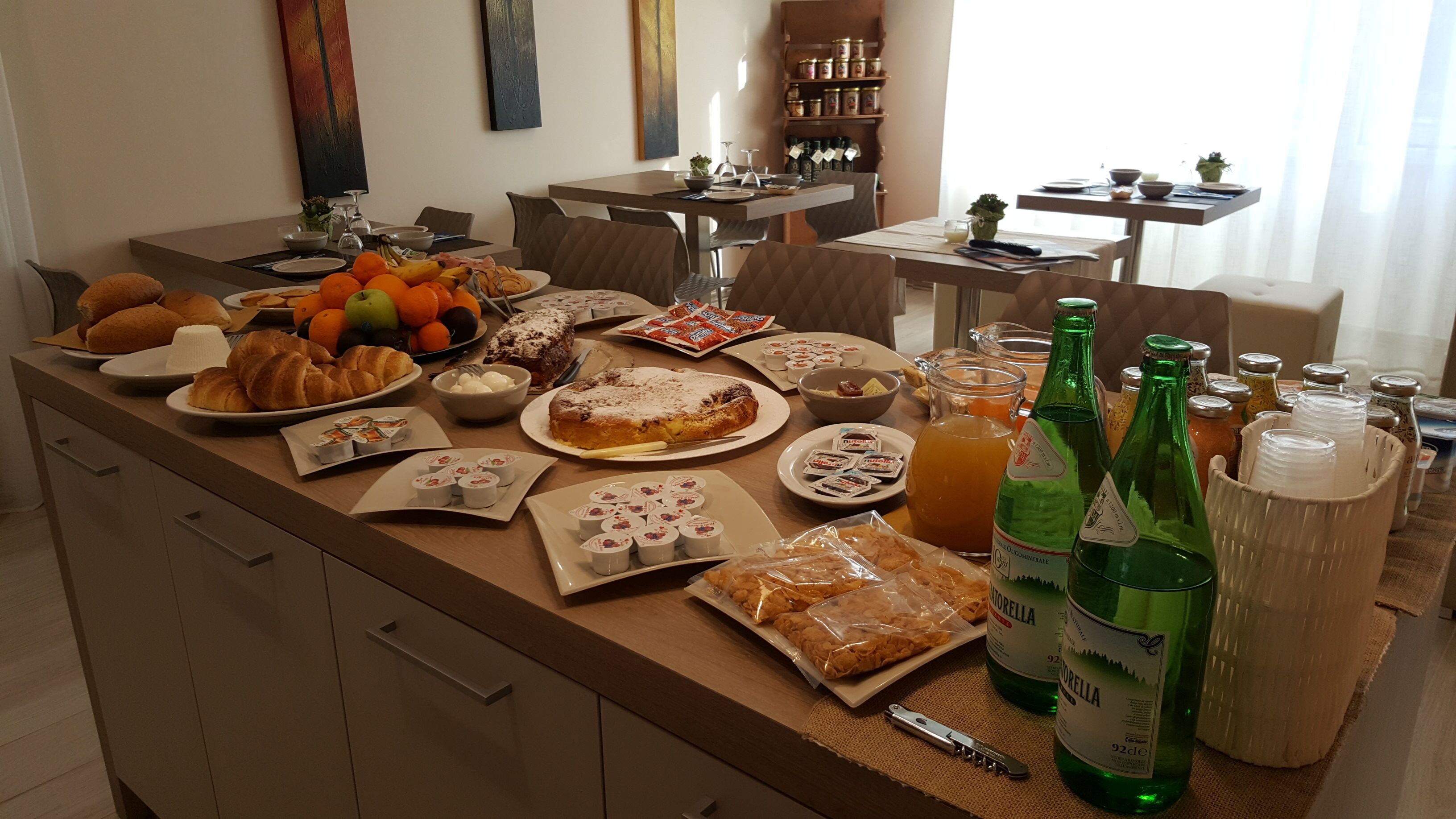 A well-equipped kitchen with various food items, including pastries, fruits, and condiments, and a dining area with chairs and a table.