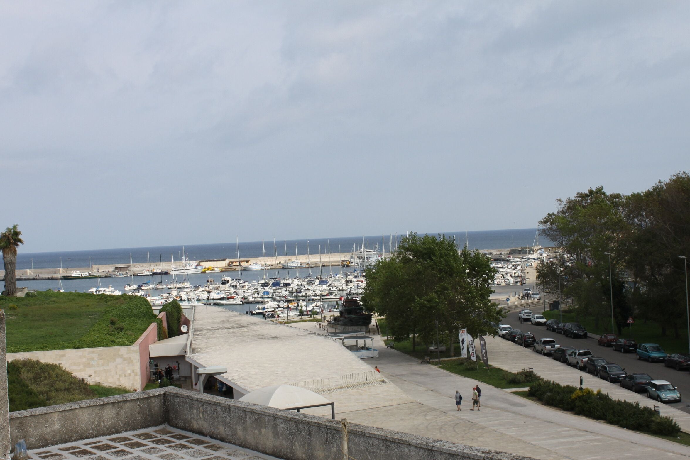 Un puerto deportivo con barcos amarrados, un paseo peatonal y vistas al mar.