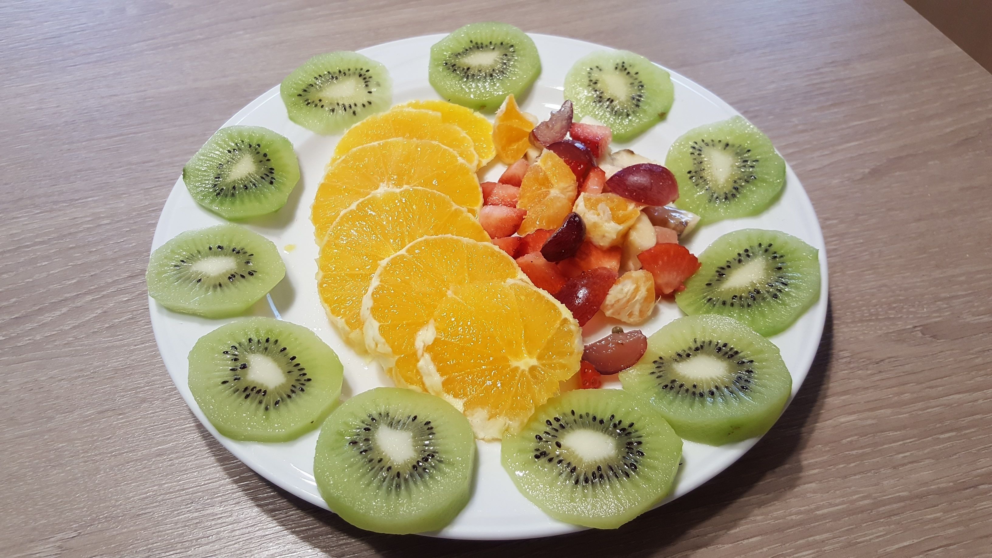 A plate of sliced kiwi and orange on a wooden table.