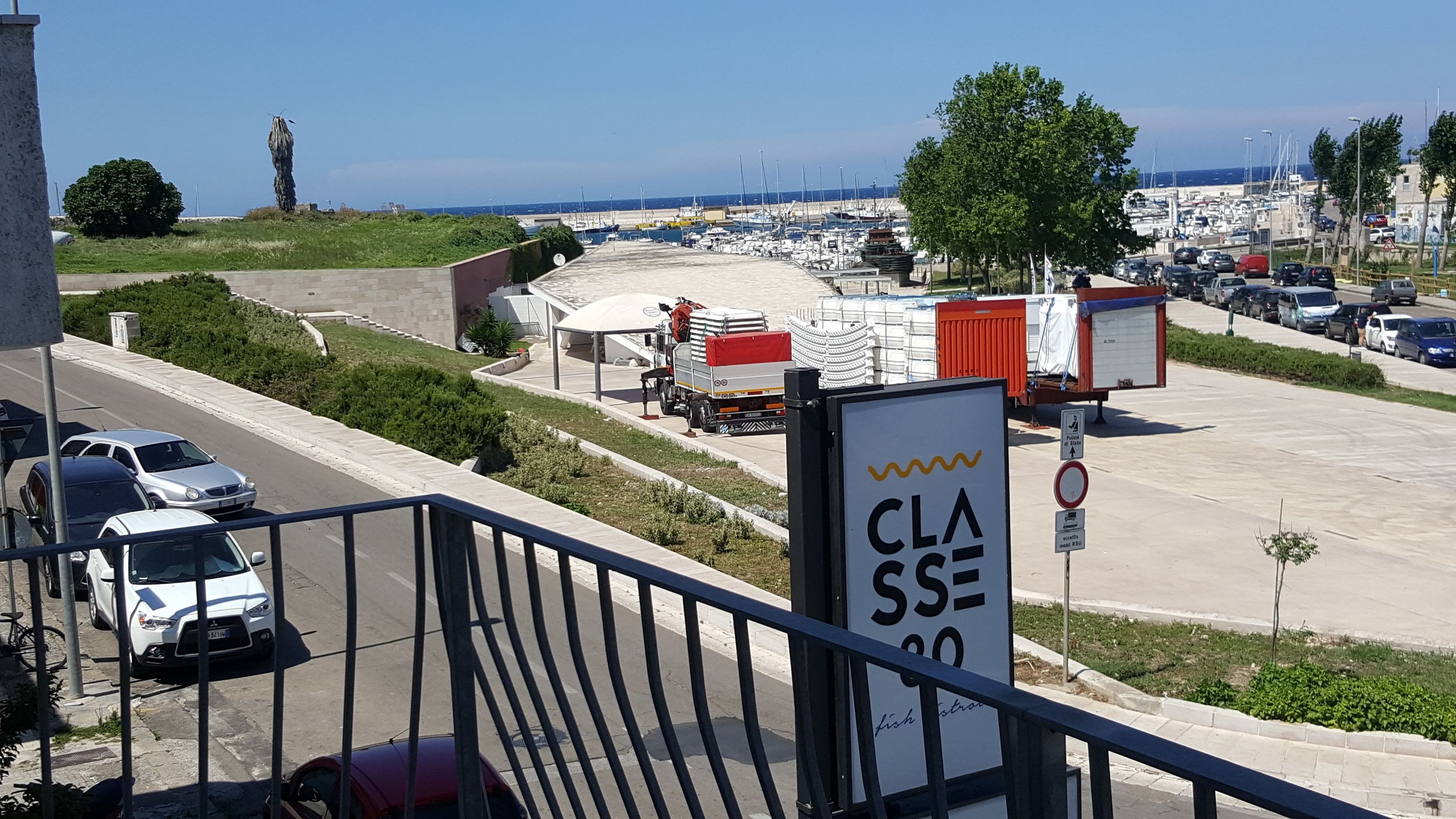 Un área de estacionamiento con un letrero que indica zona de clase 80, vista del puerto deportivo con barcos y cielo despejado.