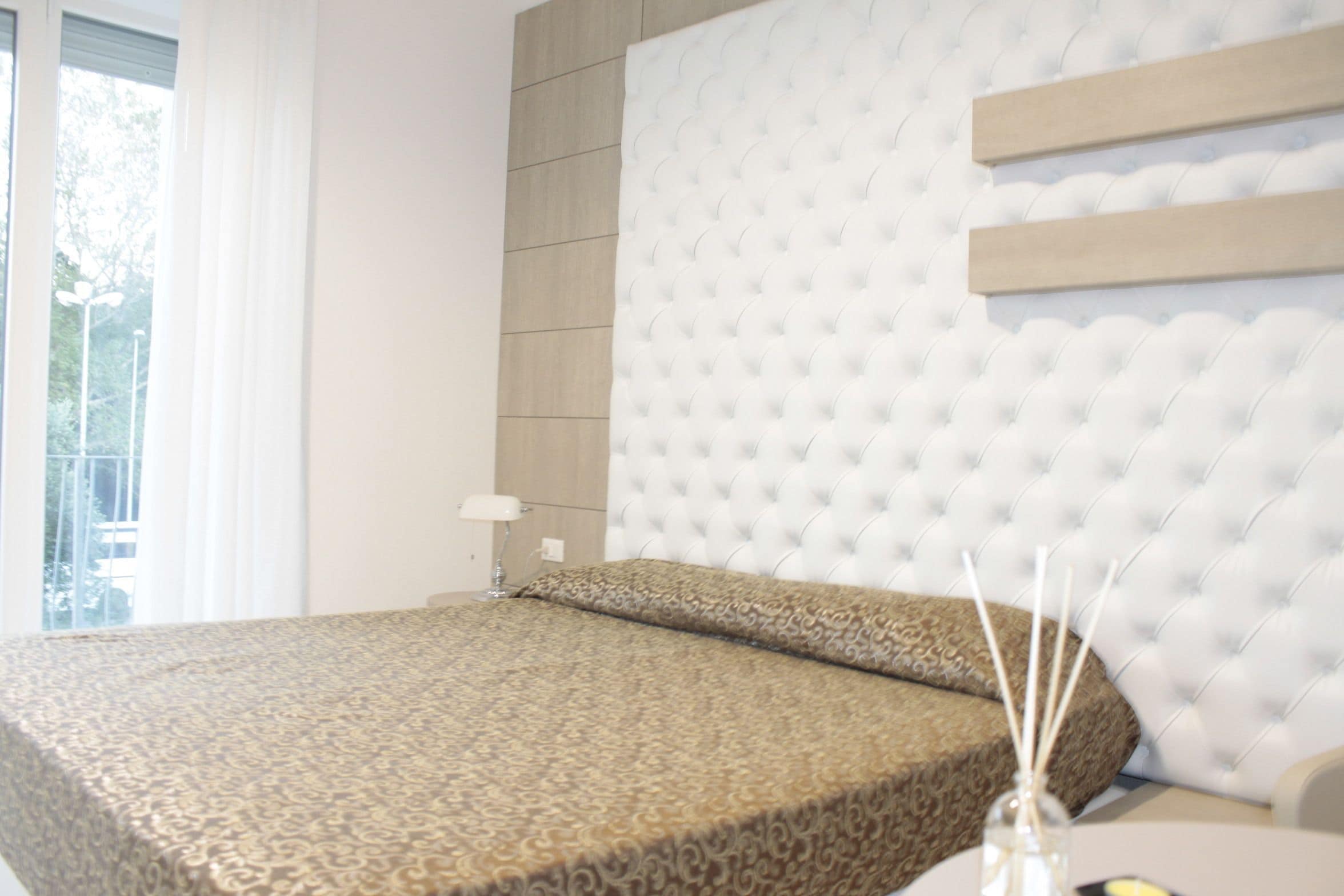 A hotel room with a tufted headboard, a patterned bedspread, and a bedside table with a lamp.