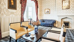 A room with a fireplace, a blue sofa, and a coffee shop menu sign. - Hotel Prince Regent (Weymouth)