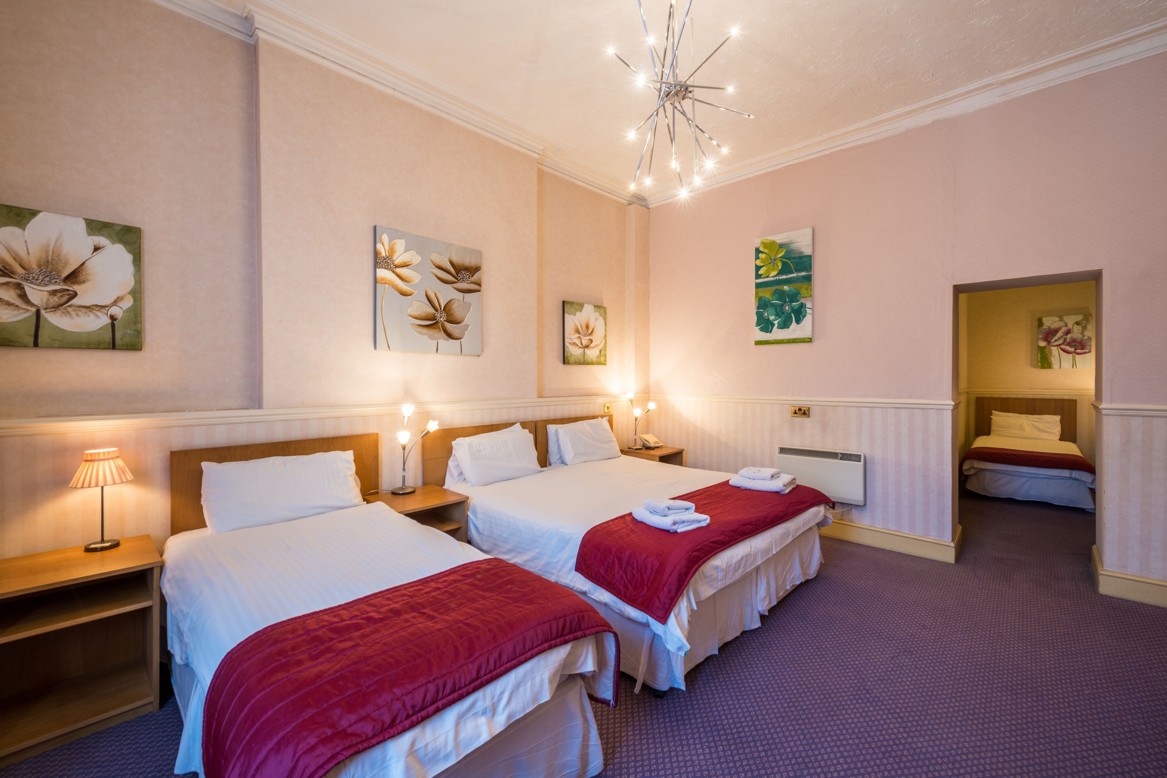 A hotel room with two beds, a chandelier, artwork on the walls, and a small seating area.