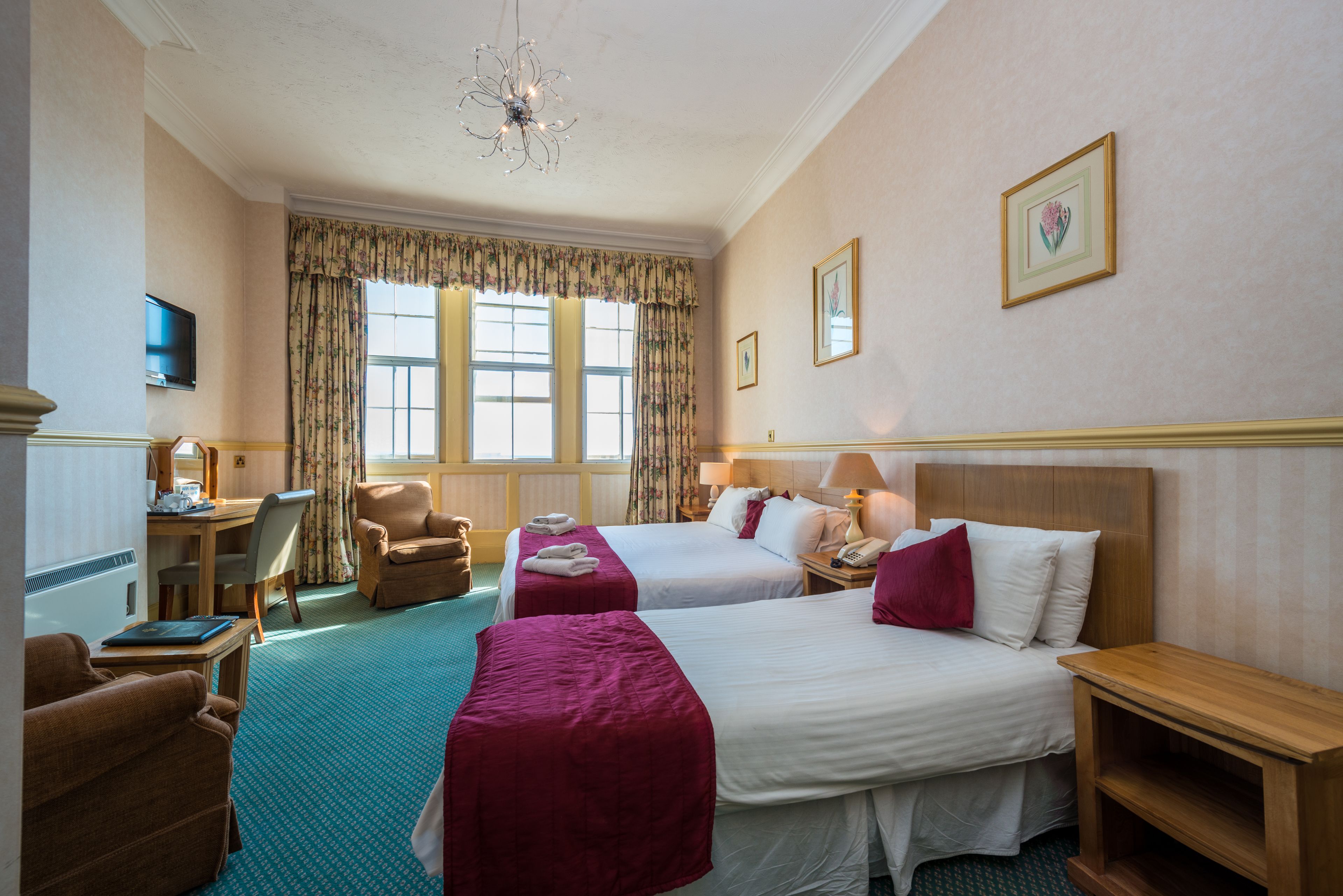 Une chambre d’hôtel avec deux lits, un bureau avec une chaise, une télévision et une grande fenêtre avec des rideaux.