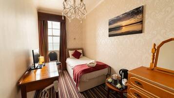 Habitación de hotel con cama, escritorio, cómoda, candelabro, pintura y ventana con cortinas.