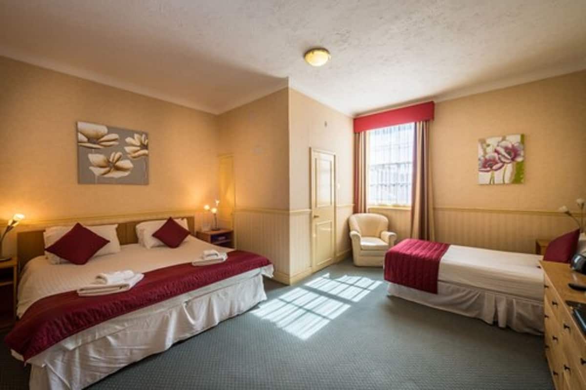 A hotel room with two beds, a chair, a dresser, and artwork on the walls.