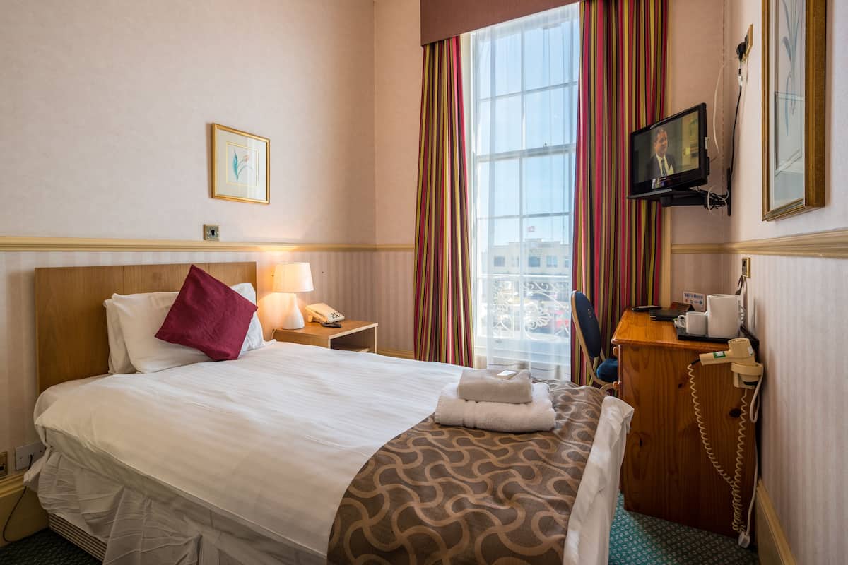 A hotel room with a large bed, a desk with a telephone, a television, and a window with curtains.