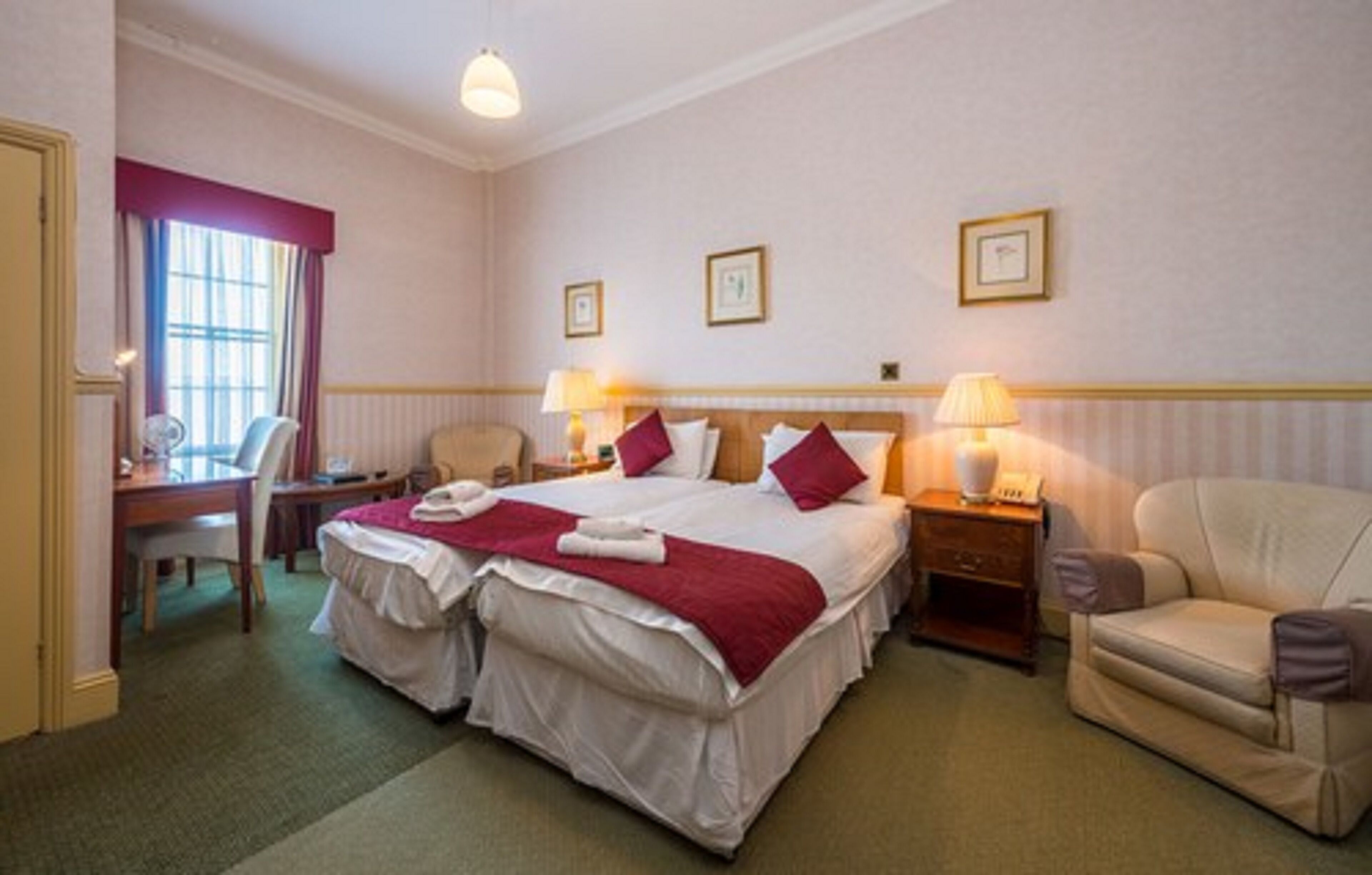 A hotel room with a large bed, two bedside tables, a chair, a desk, and a window with curtains.