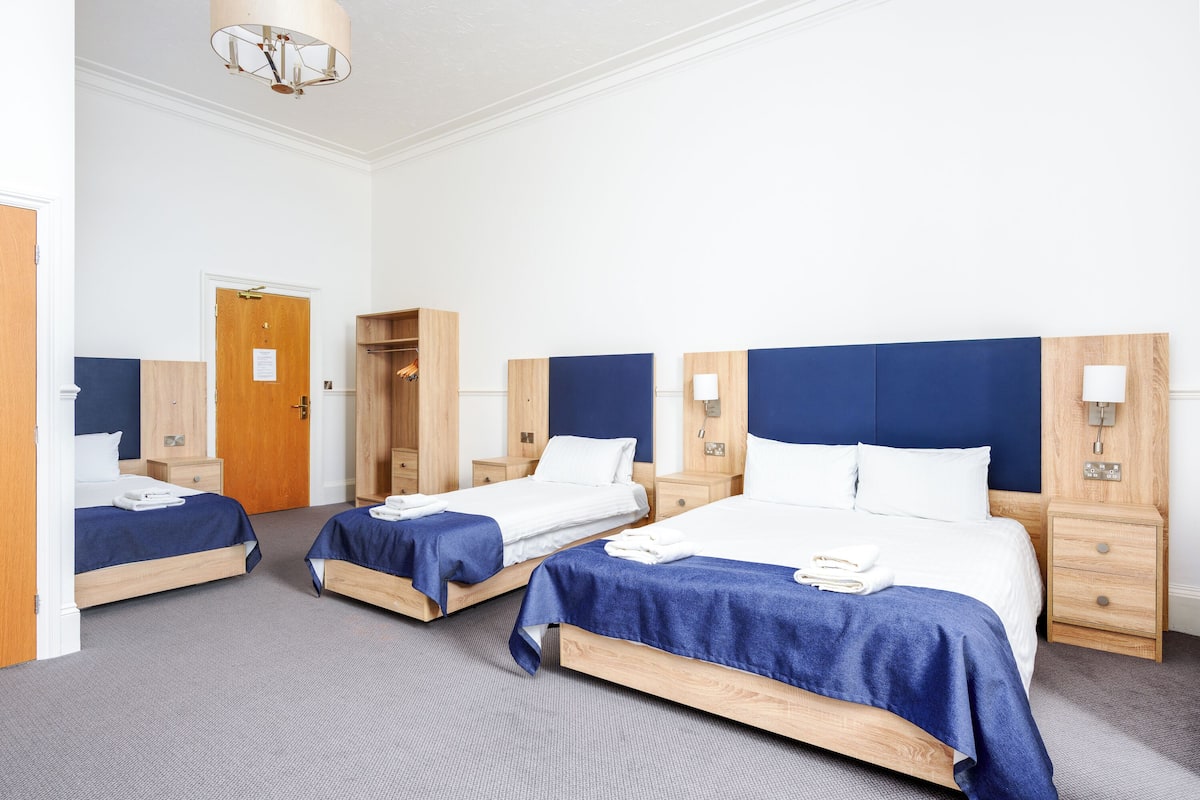 A hotel room with three single beds, wooden headboards, and a large bed with a blue headboard.
