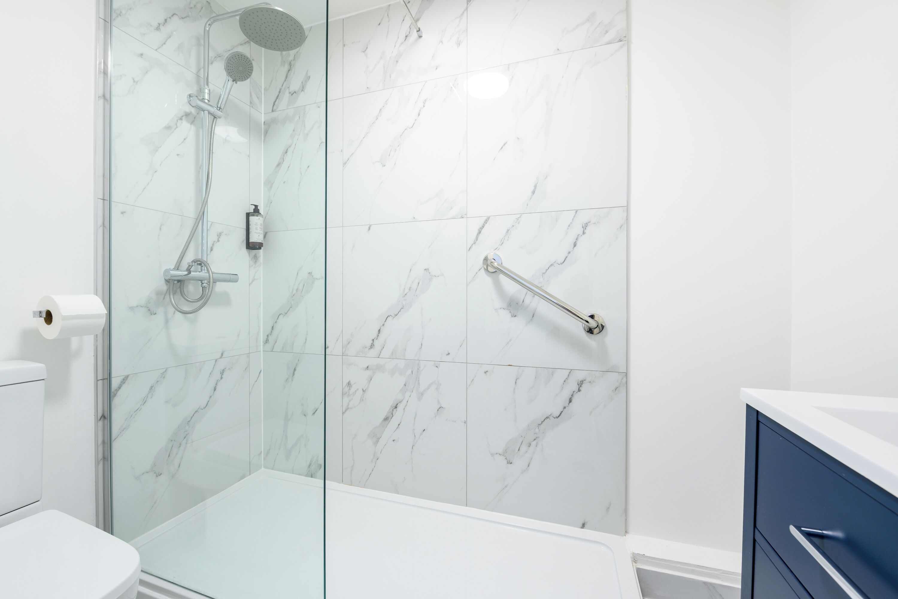 Un baño moderno con cabina de ducha de vidrio, inodoro y tocador con lavamanos.