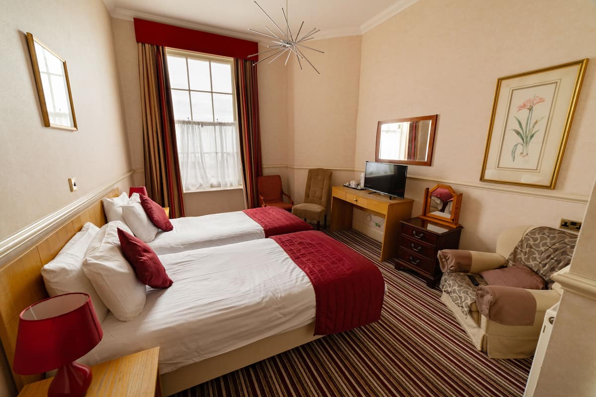 A hotel room with two beds, a desk with a television, a chair, and a small table.