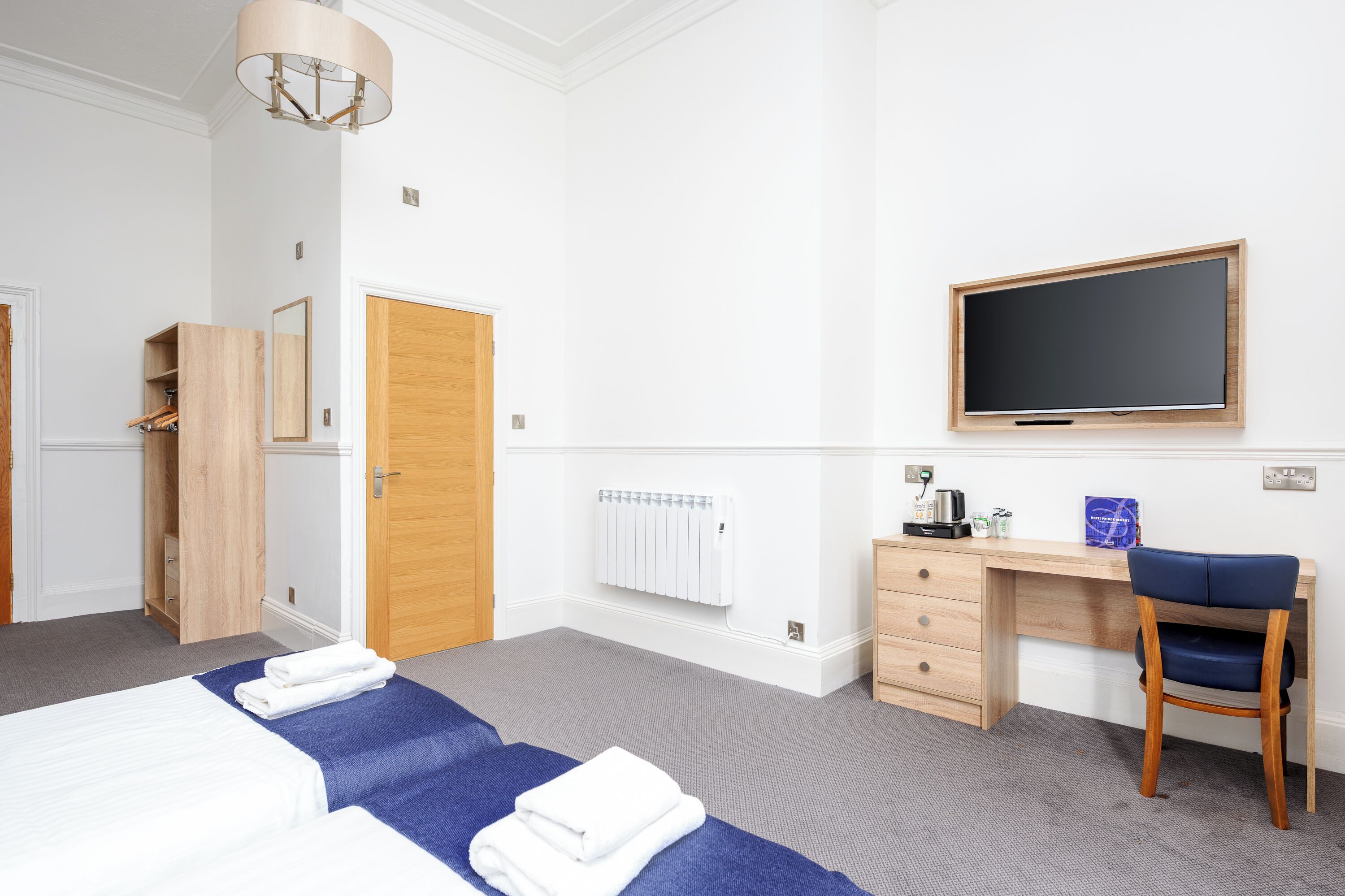 A hotel room with a bed, a desk, a chair, a flat-screen TV, and a wardrobe.