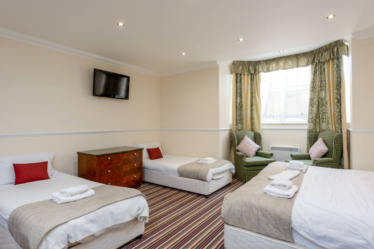 A hotel room with two beds, a TV mounted on the wall, a dresser, and a window with curtains.