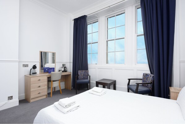 Habitación de hotel con cama, dos sillas, escritorio, espejo y ventana con cortinas.