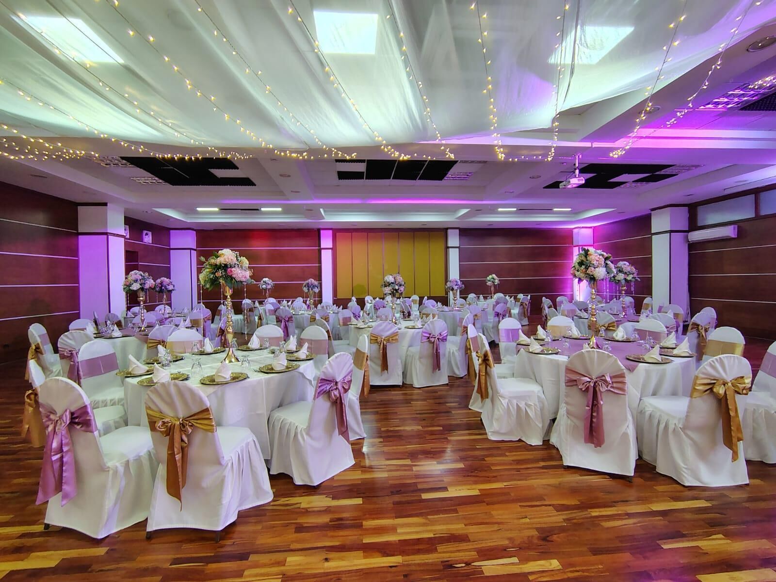 Una sala de banquets amb taules rodones, estris de taula blancs i cadires amb cintes daurades.
