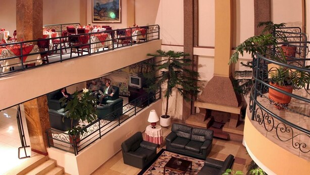 Un hall de hotel de varios niveles con un área de comedor en el piso superior, disposiciones para sentarse en el piso inferior y una escalera que conecta los niveles.