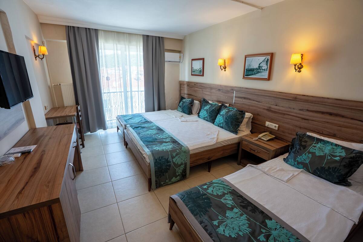 A hotel room with two beds, a wooden desk, a TV, and a balcony with curtains.