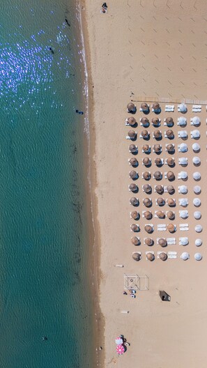 An aerial view of a beach with rows of sun loungers and umbrellas, a lifeguard tower, and a few people in the water. - Buyuk Berk Otel (Ayvalik)