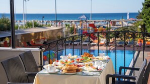 Mesa de jantar com itens de café da manhã, com vista para uma piscina e praia.