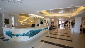 Uma área de recepção de hotel moderna, com um balcão curvo, parede decorativa azul e um lobby espaçoso com padrão de piso xadrez.