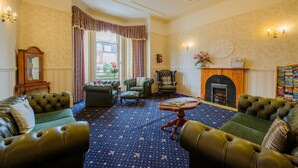 A traditional living room with leather sofas, a patterned carpet, a fireplace, and a chandelier.
