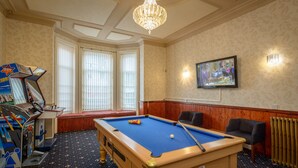 A pool table with a blue felt surface, a pool cue, and a white ball. There is a television mounted on the wall, a wooden bench, and a radiator. - Bournemouth Sands Hotel (Bournemouth)