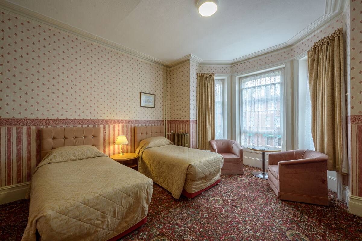 A hotel room with two beds, a sitting area with a chair and a table, and a window with curtains.