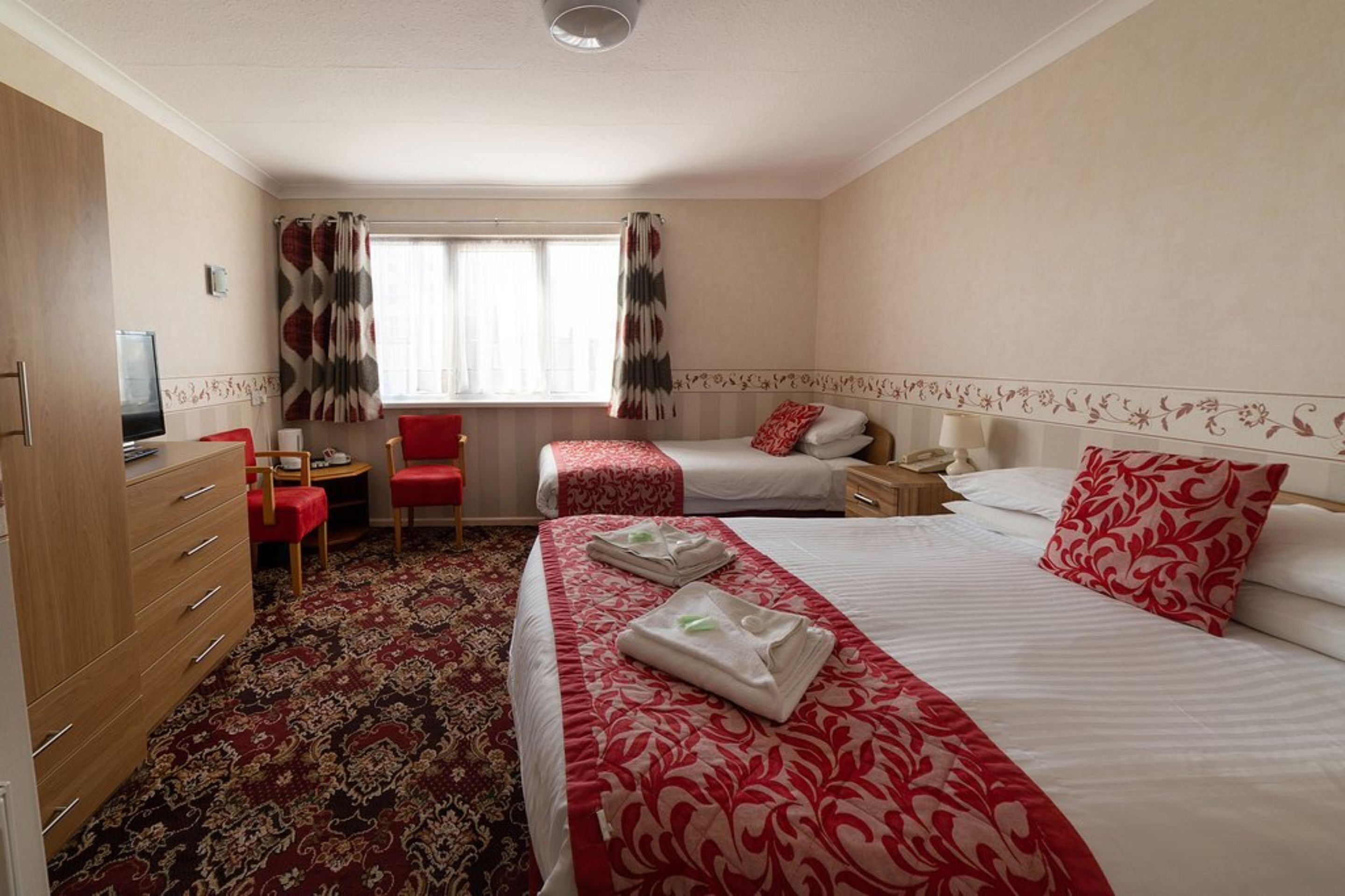 A hotel room with two beds, a desk, a chair, and a TV.
