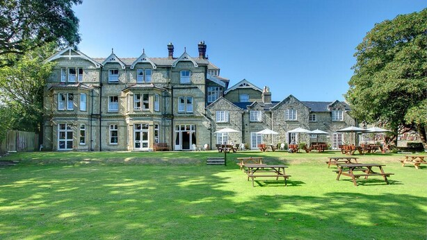 A large stone building with multiple windows and a lawn area with picnic tables. - Daish's Hotel (Shanklin)