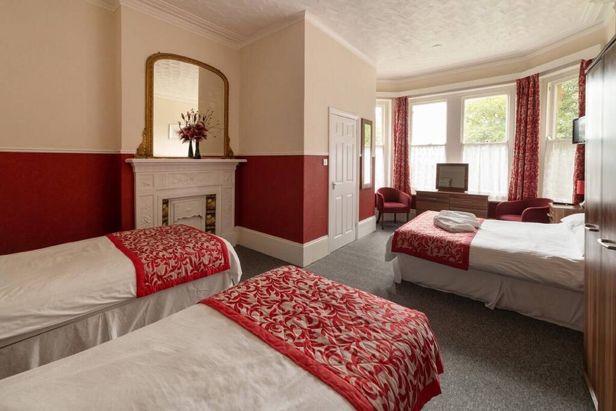 A hotel room with two beds, a fireplace, a desk with a chair, and a large window with curtains.