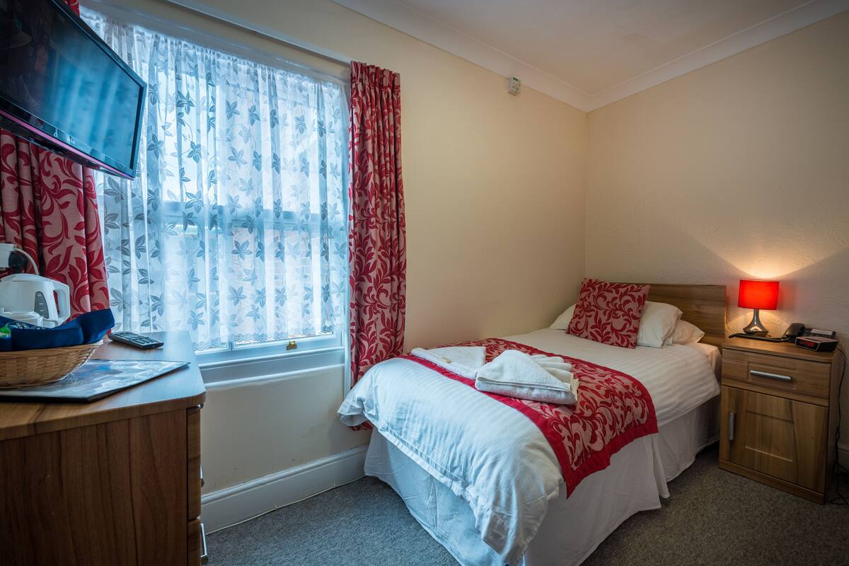 A hotel room with a bed, bedside table, lamp, and a window with curtains.