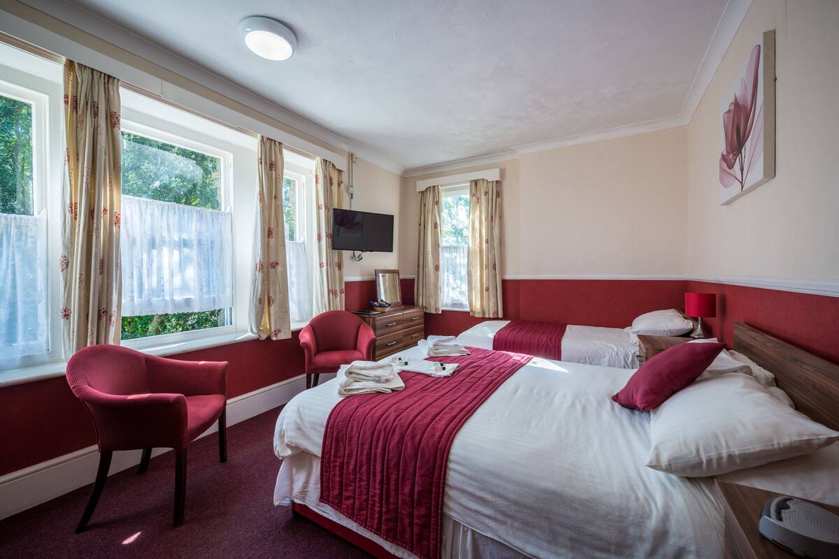 A hotel room with two beds, a TV, a red chair, and a window with curtains.