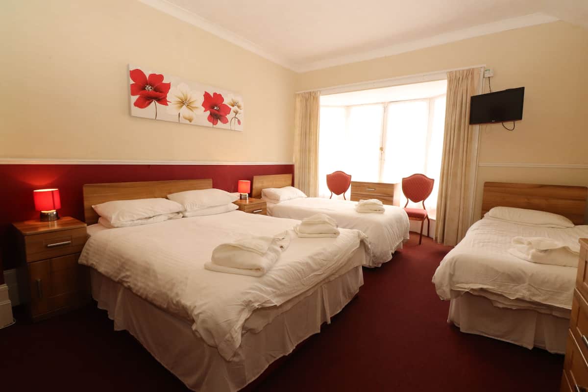 A hotel room with three beds, a TV, a red chair, and a window with curtains.