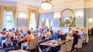 A dining area with tables and chairs, a chandelier, and a large mirror. - Daish's Hotel (Shanklin)