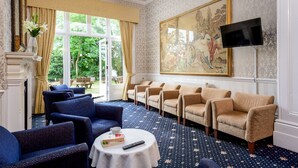 A room with a patterned carpet, a fireplace, a large window with curtains, a painting, and several sofas. - Daish's Hotel (Shanklin)