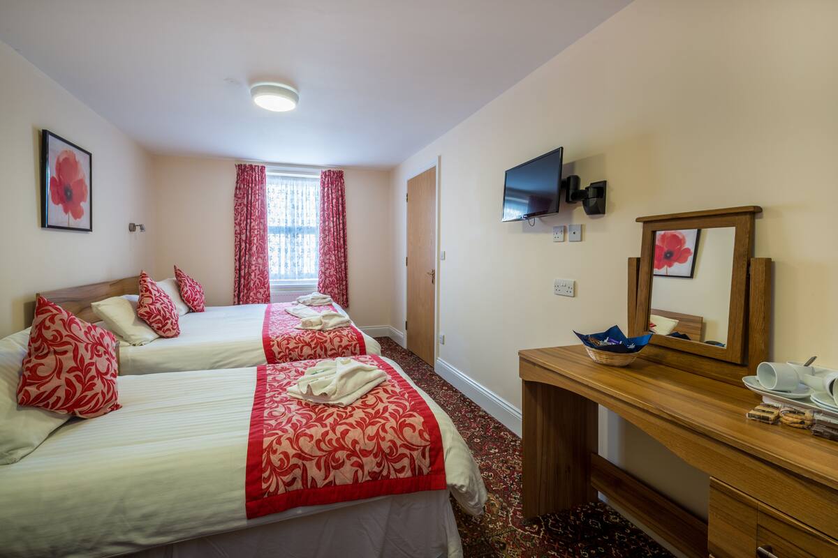 A hotel room with two beds, a wooden desk, a television, and a window with curtains.