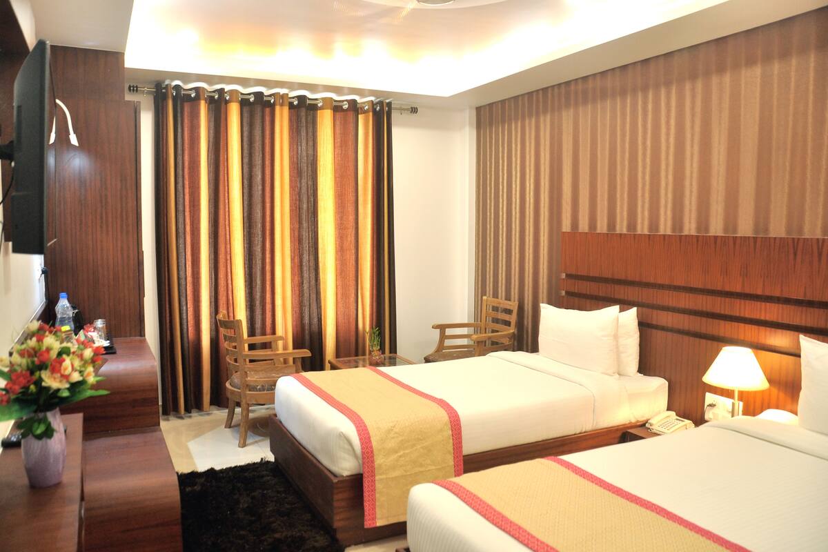 A hotel room with two beds, a wooden headboard, a desk with a lamp, a chair, and a curtain.