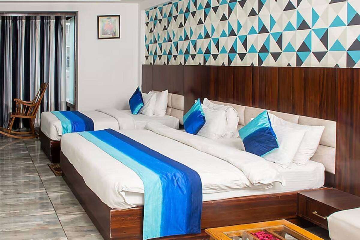 A hotel room with two beds, a wooden headboard, a patterned wall, a rocking chair, and a tiled floor.