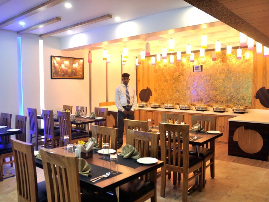 A restaurant with wooden tables and chairs, a buffet counter, and a waiter.