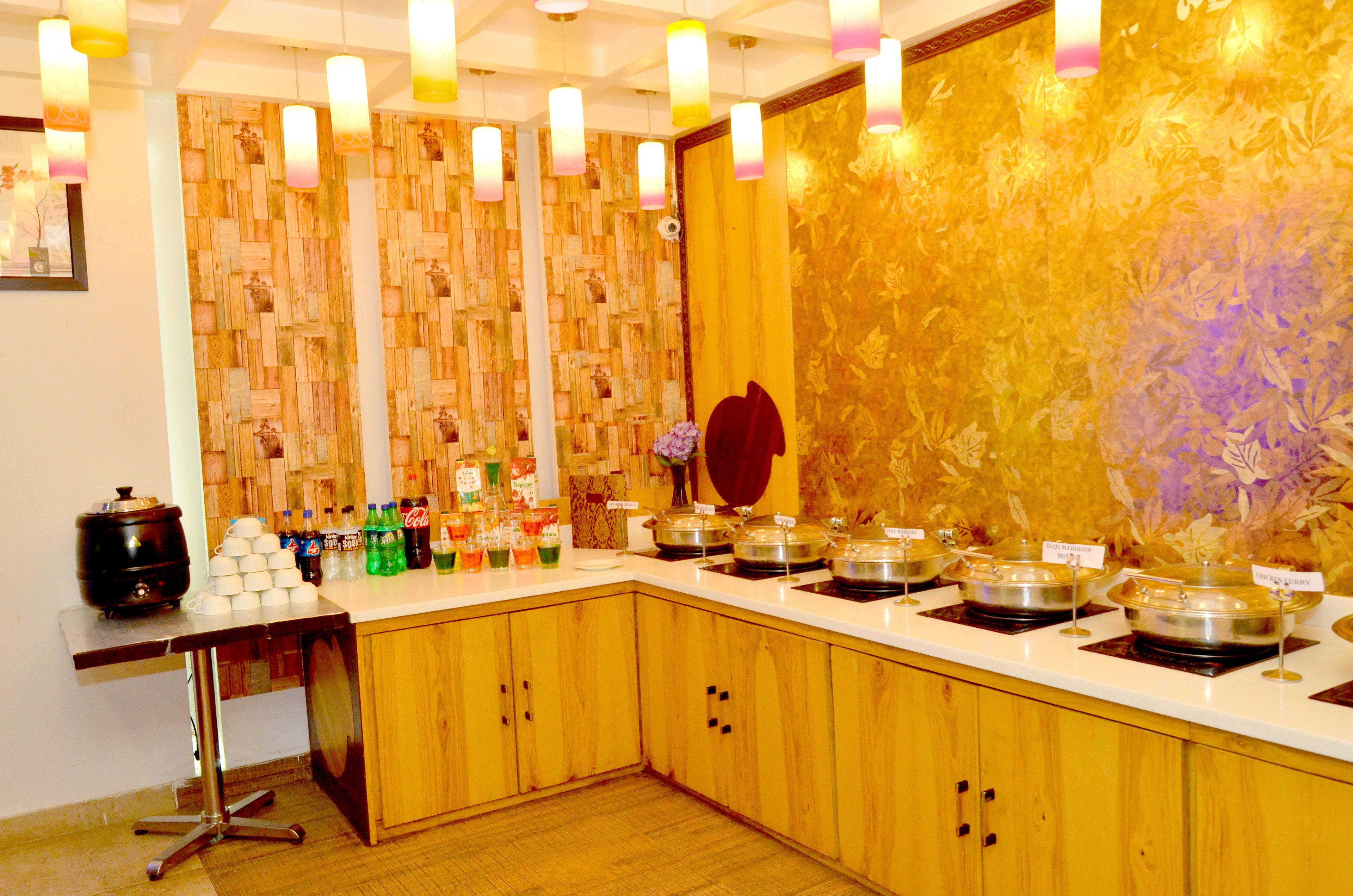 A buffet setup with various food containers and beverages, a wooden cabinet, and a table with a stand.