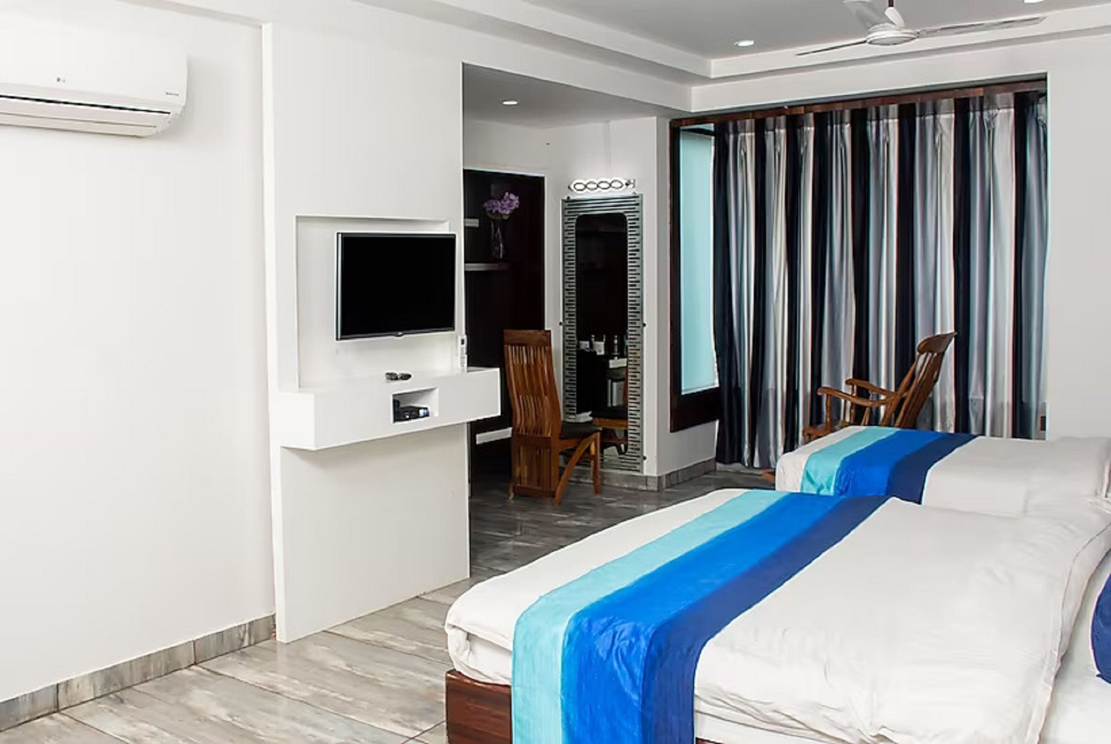 Ein Hotelzimmer mit zwei Betten, einem Fernseher, einem Schreibtisch und einem Spiegel.
