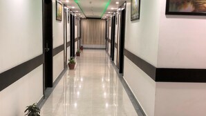 A long, well-lit hallway with a reflective floor, potted plants, and framed artwork on the walls. - Hotel SGT Plaza (Varanasi)