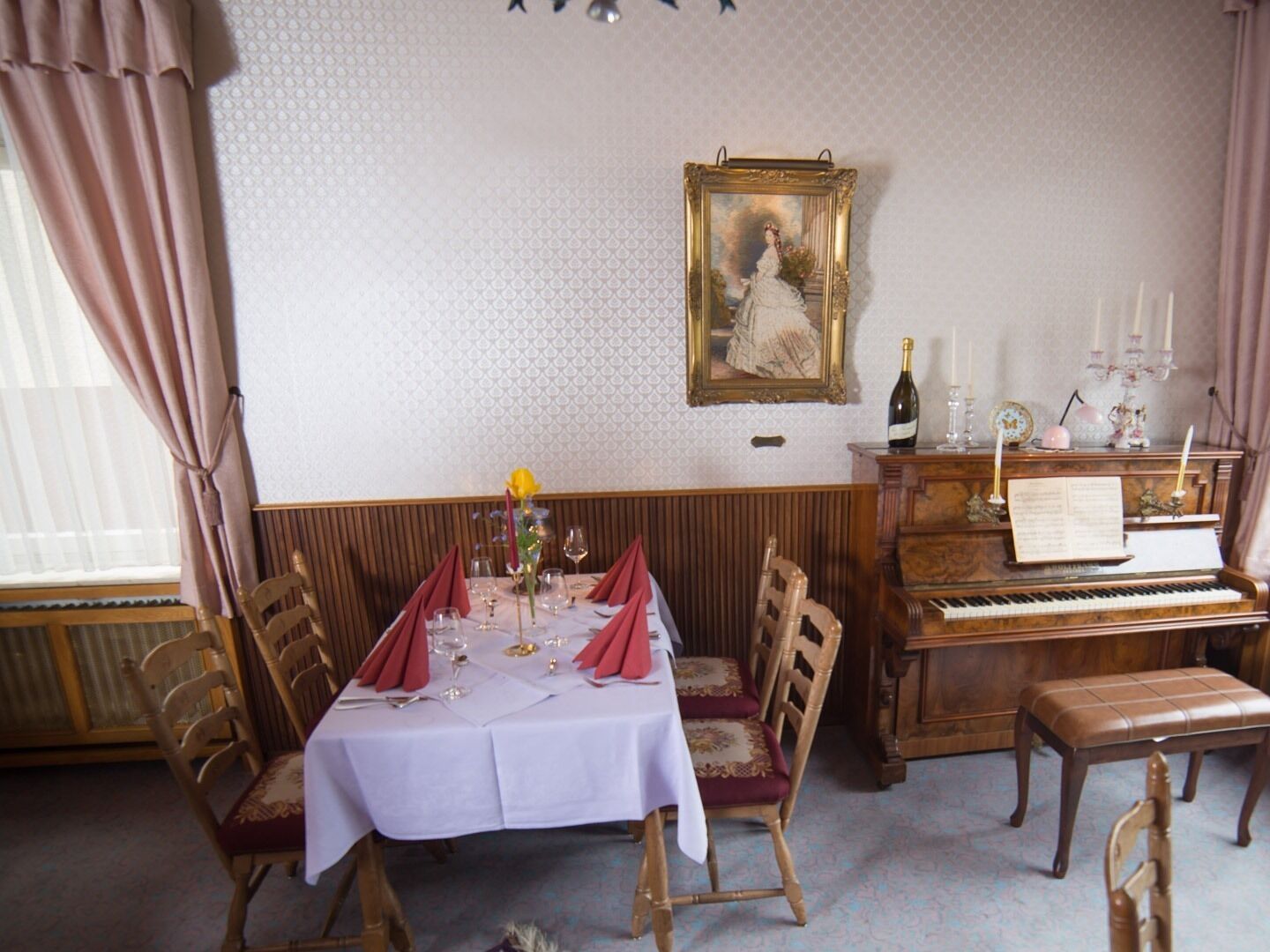 Uma sala de jantar com mesa posta para quatro pessoas, um piano e um quadro emoldurado na parede.