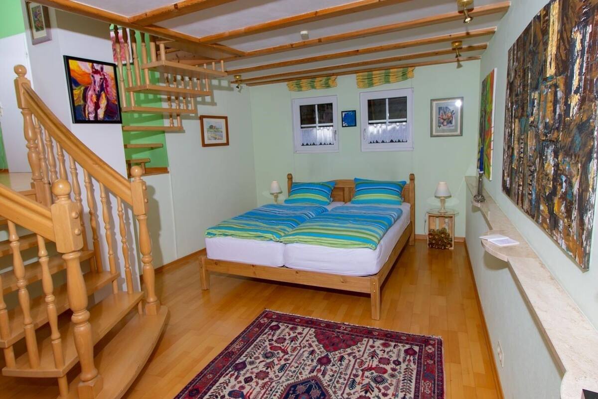 Quarto com cama de madeira, escada de madeira e uma grande pintura abstrata na parede.