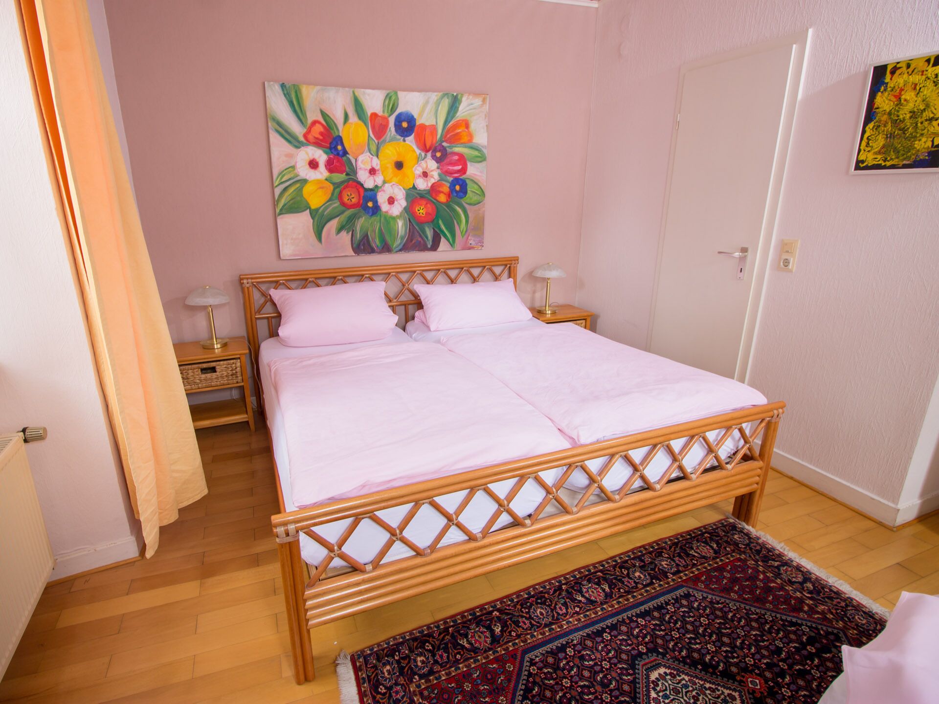 Une chambre à coucher avec un lit en bois, deux tables de chevet, une commode, un tableau coloré et un tapis à motifs.