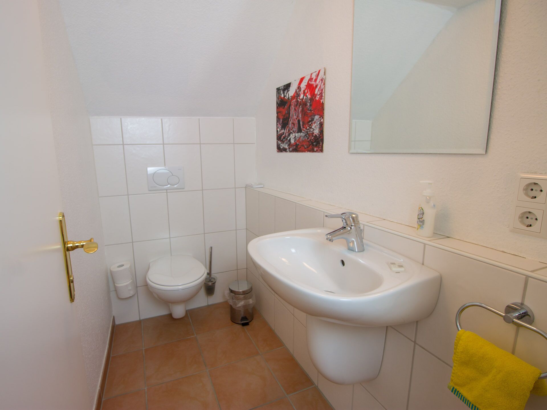 A bathroom with a white sink, a toilet, a trash bin, and a yellow towel on a rack.