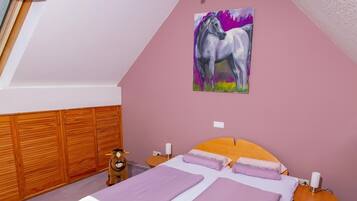 A bedroom with a sloped ceiling, a bed with purple bedding, a wooden wardrobe, a small wooden nightstand, a wall-mounted painting of a horse, and a window with a wooden blind.